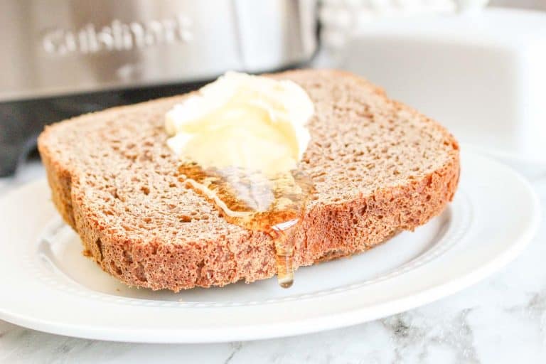 Honey dripping from a buttered slice of honey wheat bread on a white plate.