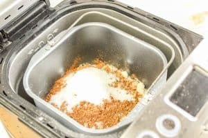 Bread machine pan filled with flour, cocoa powder, sugar, and dry ingredients for honey wheat bread.