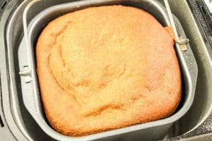 Freshly baked honey wheat bread loaf inside a bread machine pan.