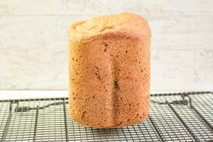 Tall loaf of honey wheat bread cooling upright on a wire rack.